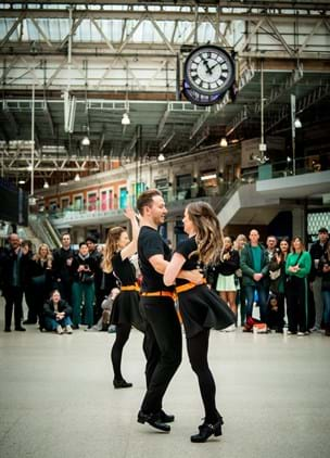 Irish dancers in the middle of a train station smiling and clapping