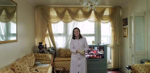 A person standing in their living room in front of a window, with sofas around them