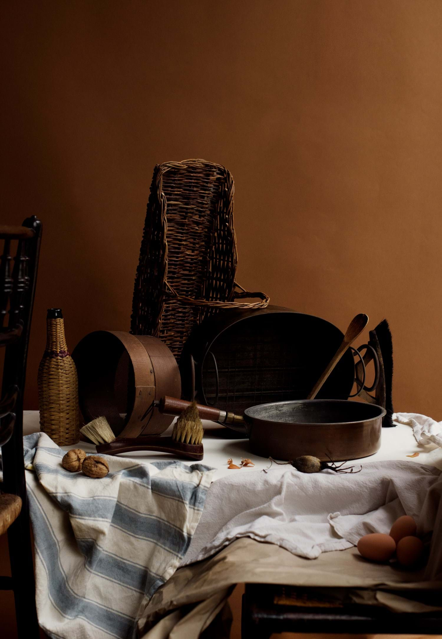 A wooden table topped with tablecloth and kitchen fabrics. On top of the table are different items used in a Tenement Flat in 1913 in a Jewish household including a pan and a frying pan. The overall tone is brown.