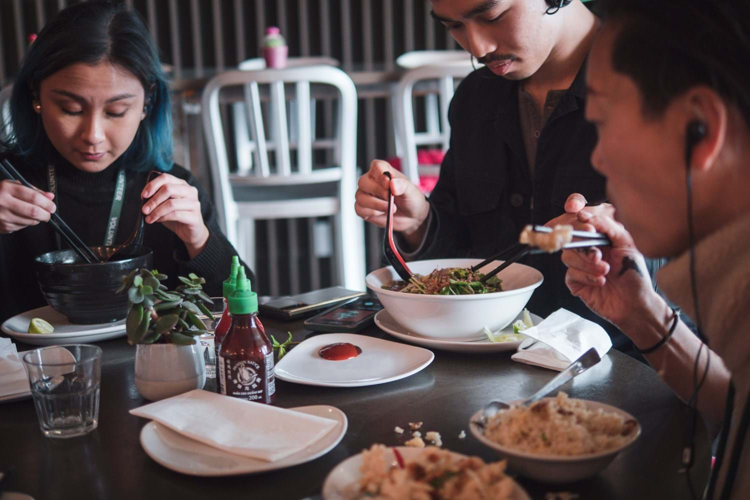 People wearing earphones while eating bowls of noodle soup in a restaurant