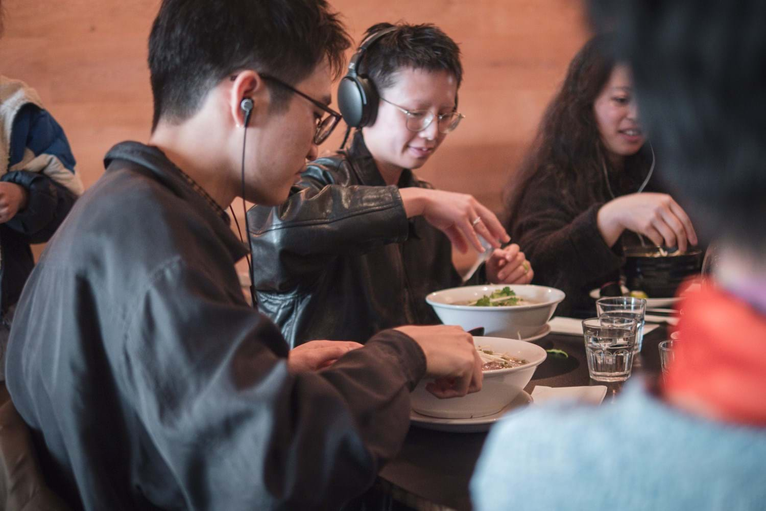 People wearing earphones while eating bowls of noodle soup in a restaurant