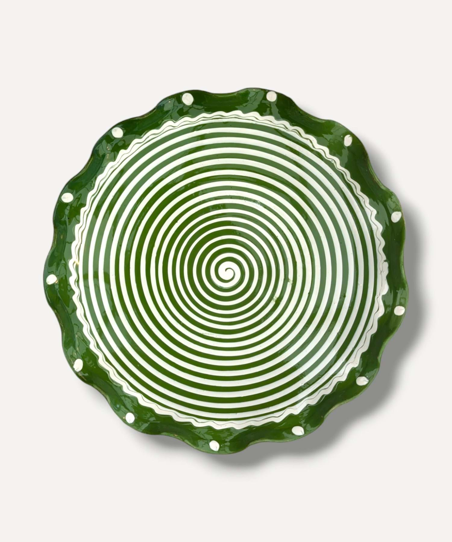 A hand painted plate with a green spiral pattern and frilled edges