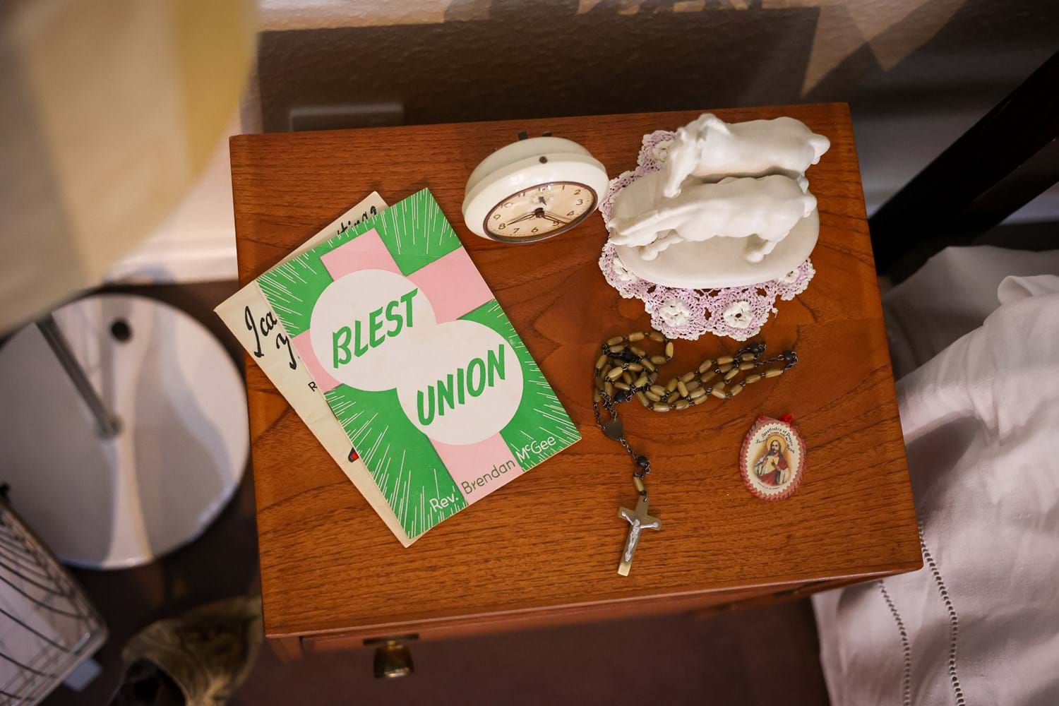 Objects laid out on a wooden bedside table, including praying beads and a green and pink brochure with the words "BLEST UNION"