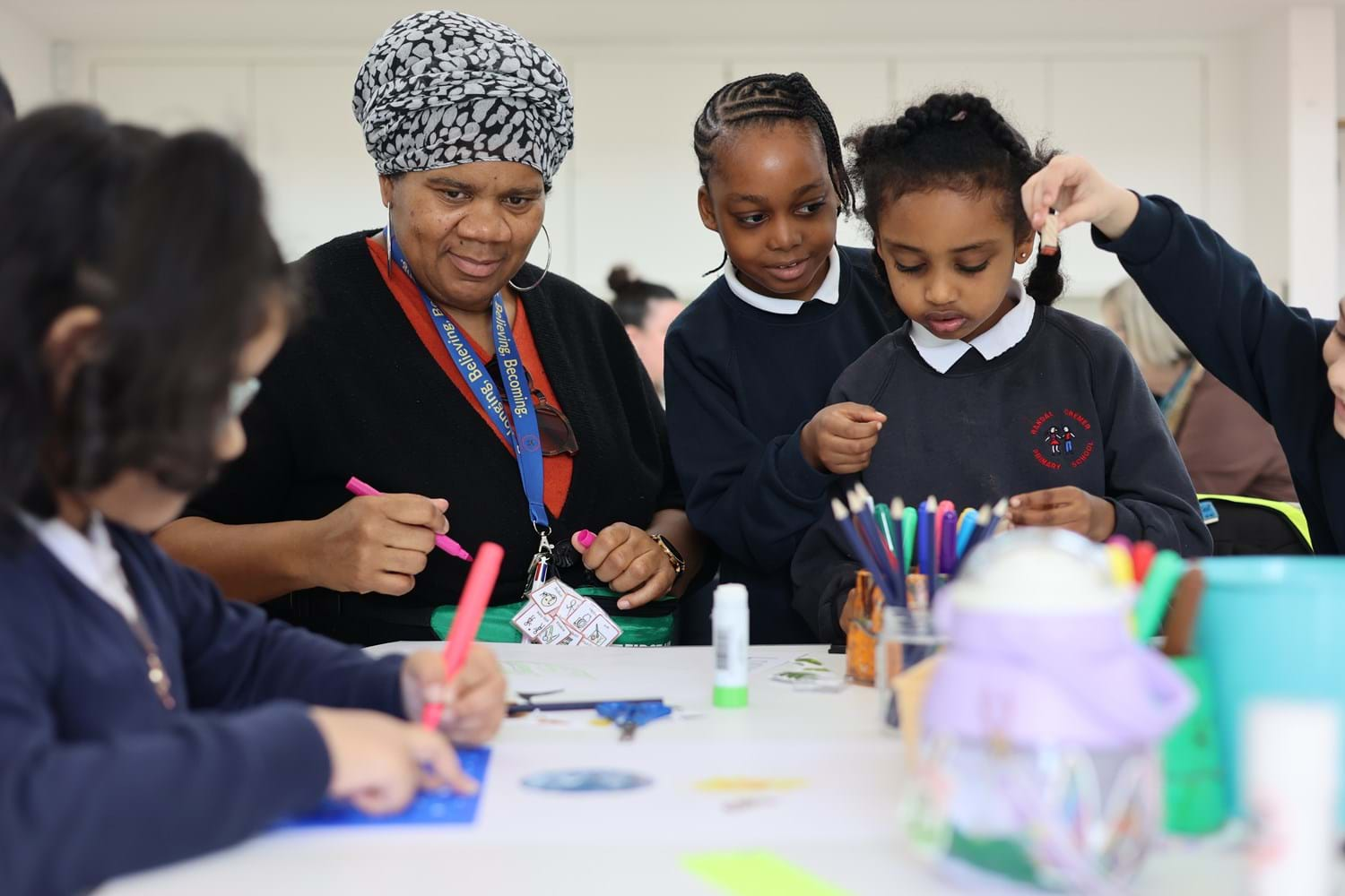 An adult helping three school children in uniform during an art craft workshop.