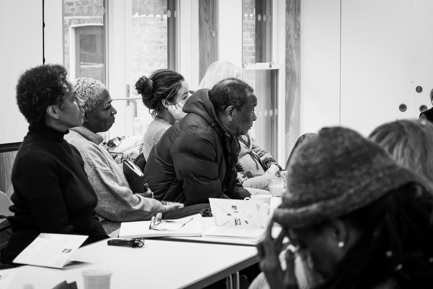 A black and white photograph of a group of people in discussion by a desk.