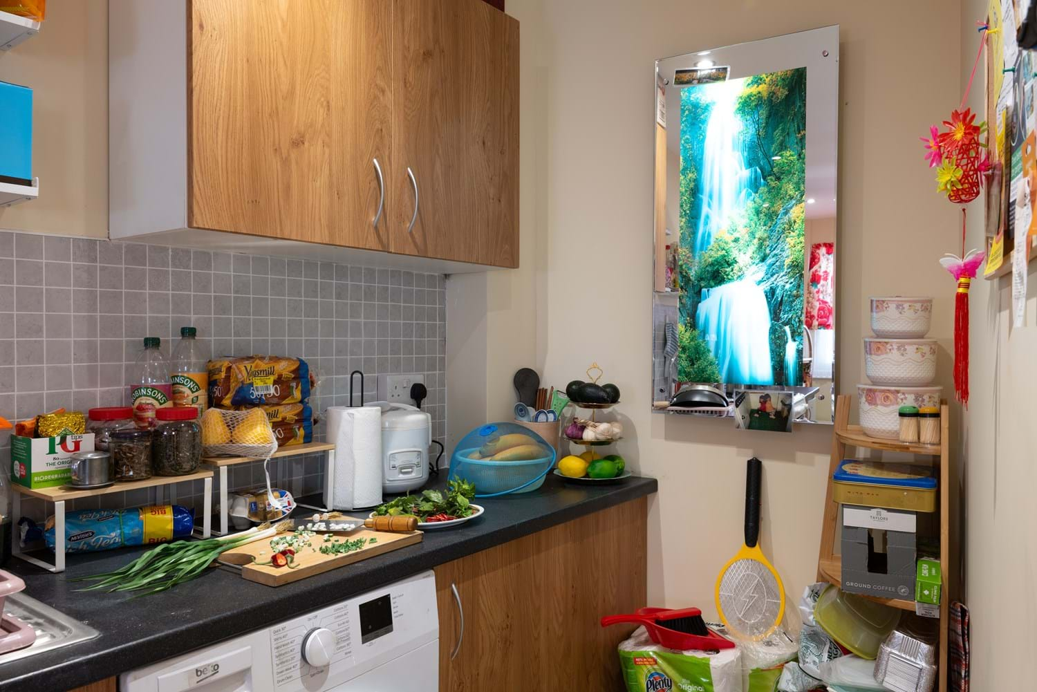 A shot of the kitchen in a British-Vietnamese home in A Terraced House in 2024, the one of the rooms in Rooms Through Time at Museum of the Home. It has different cooking ingredients, classic waterfall mirror, zapper, etc.