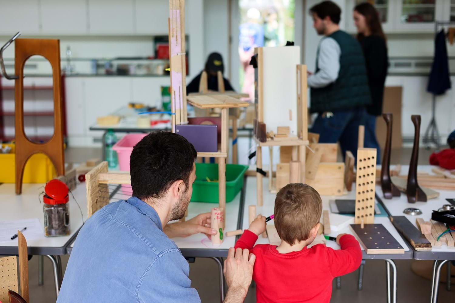 An adult and a child are building an architectural structure with wooden blocks of various shapes.