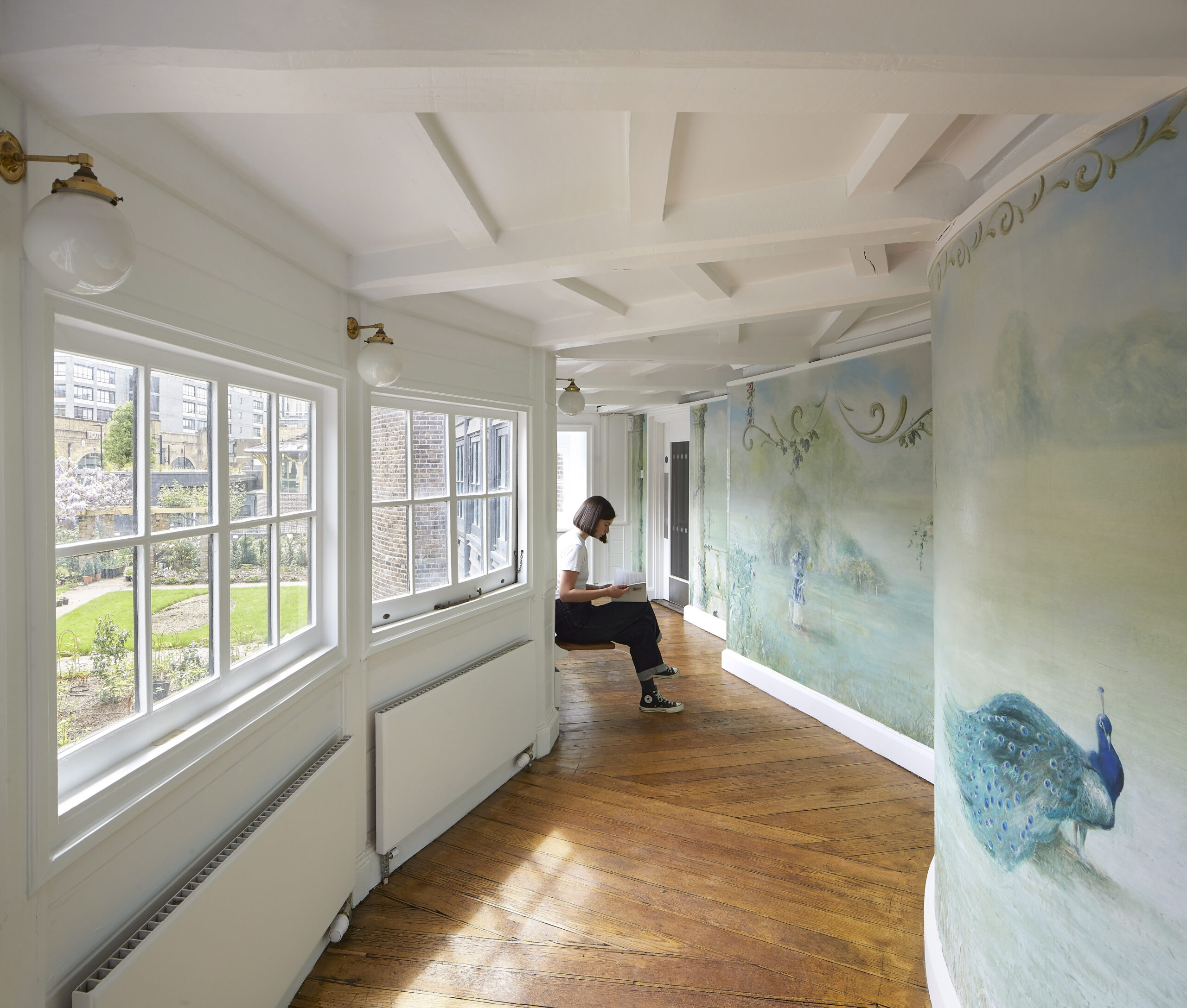 a person sitting in a curved reading room that overlooks a garden and has blue painted impressionist wallpaper