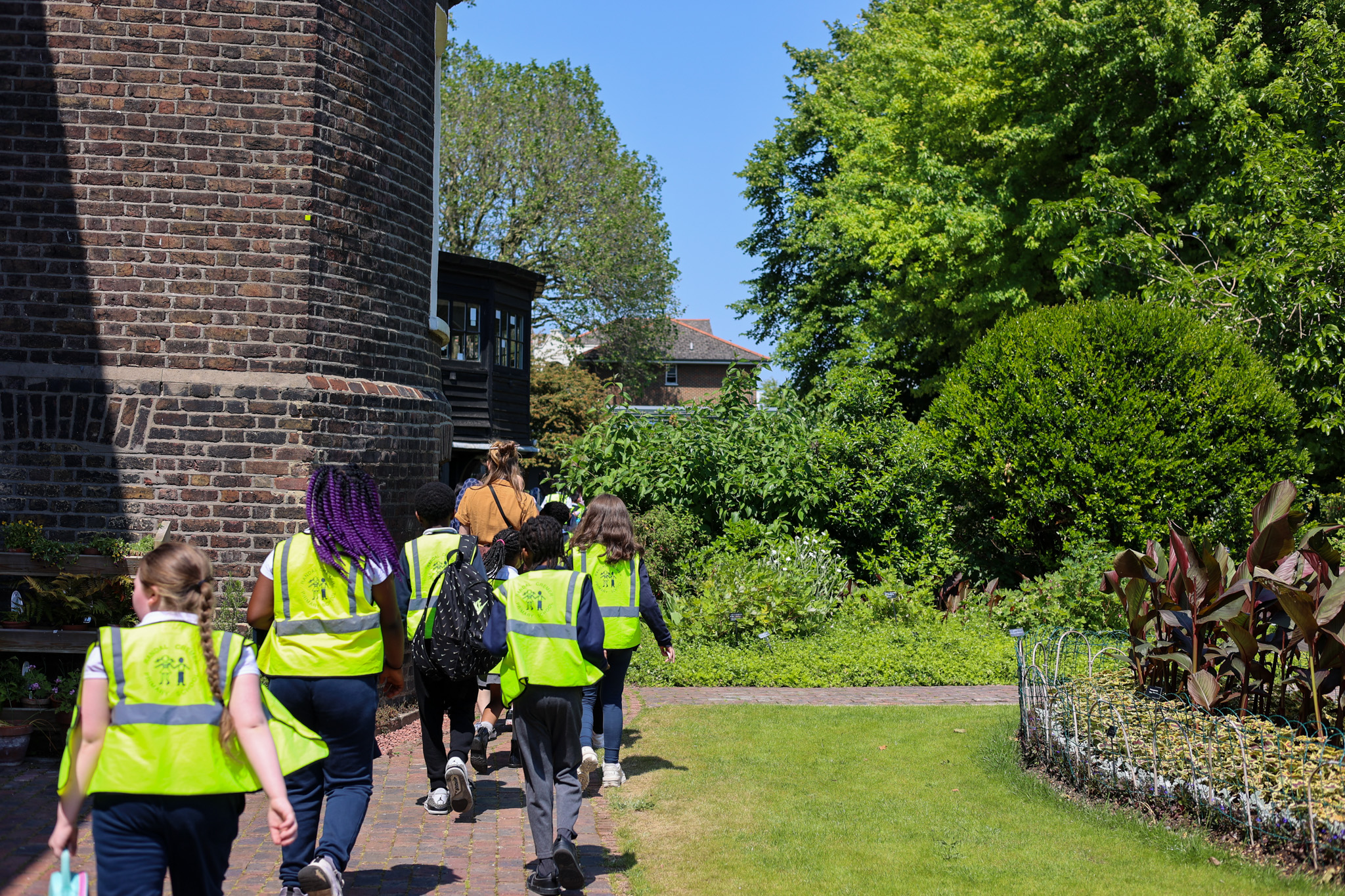 A group of children in yellow vests run through a green garden