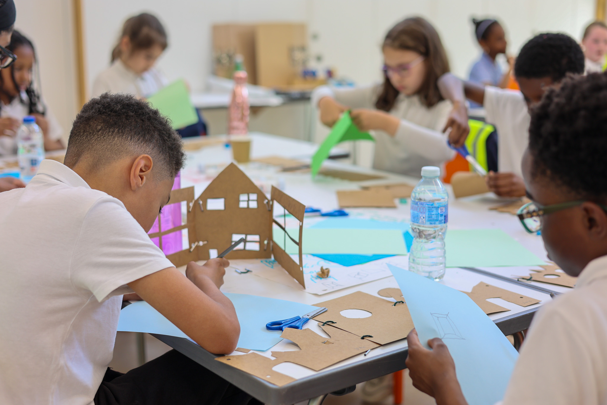 School children sit around a table working on crafts and cutting paper to make paper houses