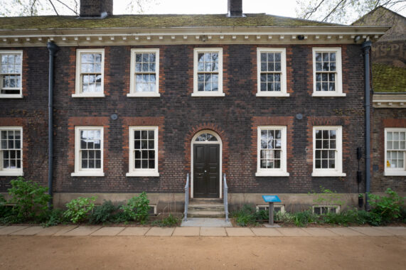 Exterior of a brick building with symmetrical white-trimmed windows, arched doorway, and moss-covered roof