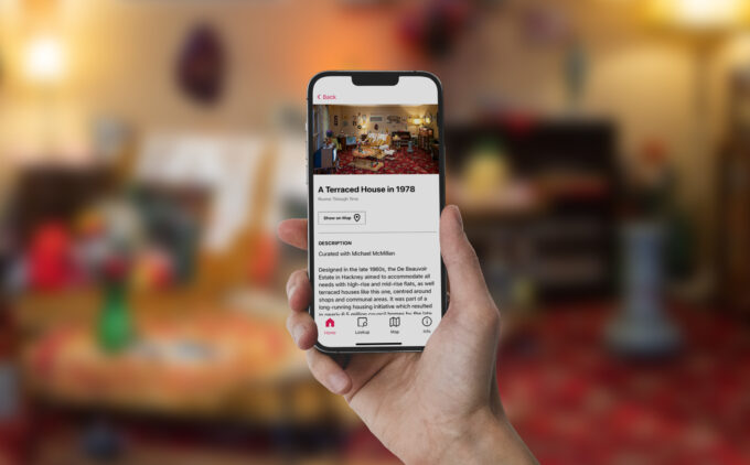 A hand holding up a smartphone displaying information and an image of a terraced house from 1978, with the actual display blurred in the background.