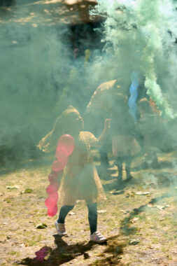 A blue green smoke fills an outdoor space, a child is just visible looking up