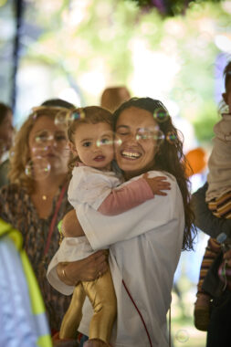 A woman holds a child smiling as bubbles move in front of them.