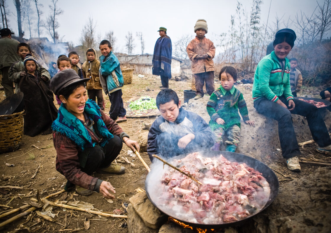 A family gather around a large pot of meat smiling