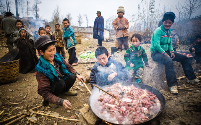 A family gather around a large pot of meat smiling