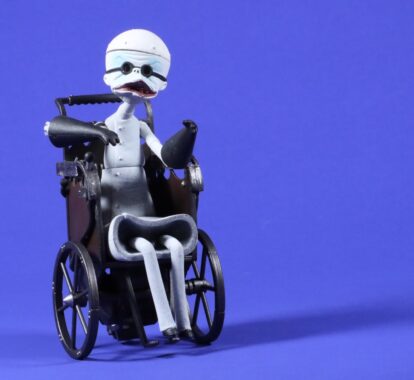 A stylised action figure of Dr. Finkelstein from The Nightmare Before Christmas, featuring a white skeletal body, black gloved hands, and a dark wheelchair, placed against a purple-blue background.