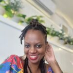 A black woman smiles at the camera wearing a colourful, floral shirt.