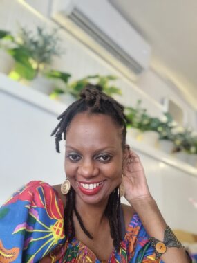 A black woman smiles at the camera wearing a colourful, floral shirt.