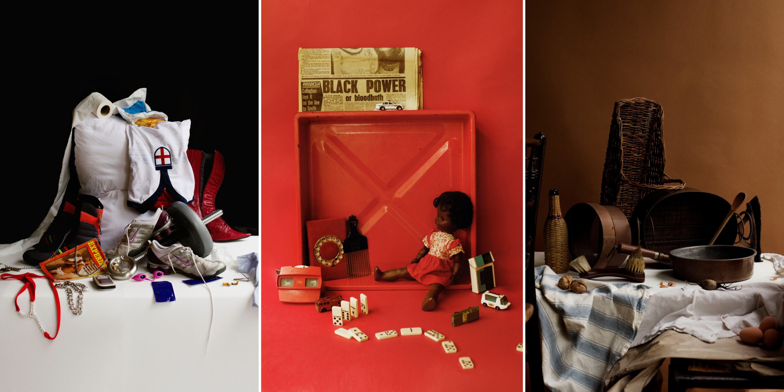 This image shows three distinct still life arrangements displayed side by side. On the left Modern items including a white pillow, red boots, england shirt, and other items tumble down. In the centre, toys, dolls, dominoes, and a newspaper reading "Black Power or bloodbath" arranged in a red display case. On the right, woven baskets, pottery, and wooden implements on cloth against a brown background.