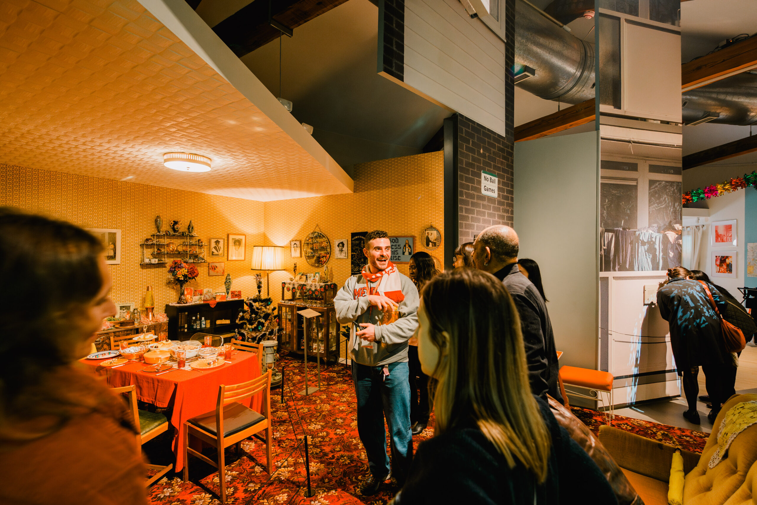A person smiling while taking people on a tour of a 1970s room set in a gallery