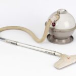 White-and-beige spherical Hoover Constellation vacuum cleaner on a white background: its ball-shaped body with a carry handle and red Hoover logo feeds a flexible beige hose and straight silver tube, ending in a white plastic floor nozzle.