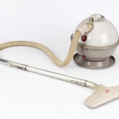 White-and-beige spherical Hoover Constellation vacuum cleaner on a white background: its ball-shaped body with a carry handle and red Hoover logo feeds a flexible beige hose and straight silver tube, ending in a white plastic floor nozzle.