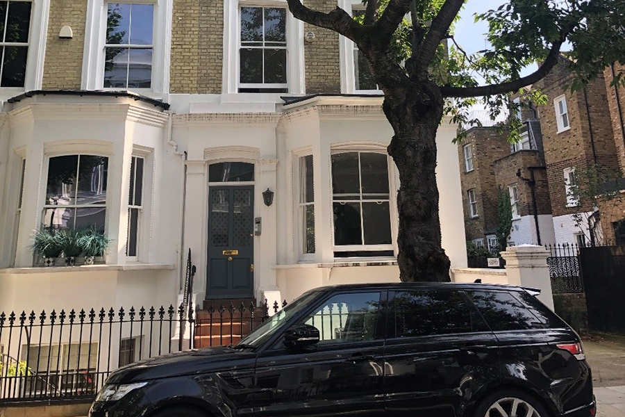 A car and tree in front of a house with a central door flanked by two bay windows.