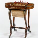 Inlaid chess table with red and white pieces, curved legs, and cream, fabric storage pouch.