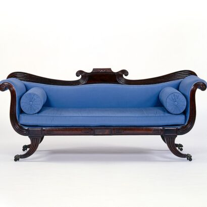 Dark wood settee with blue upholstery on tapered legs with curved arms and decorative carved details.
