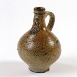 Stoneware jug with bearded face decoration, round body, spotted brown glaze and single handle.