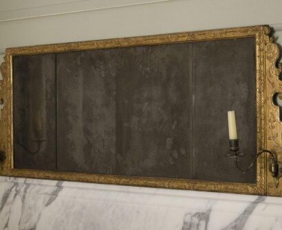 Gilt-framed horizontal mirror with candle sconces mounted on a marble surface.
