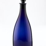 Dark blue tapered glass decanter with pear shaped black stopper.
