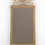 Gilt-framed vertical mirror decoratively surmounted by a vase.