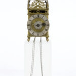 Brass and metal decorative clock with a domed top on four ball feet and two hanging chain weights.