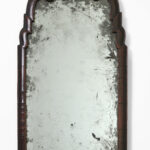 A mirror with dark wooden frame featuring scrolled details and an aged, distressed reflective surface.