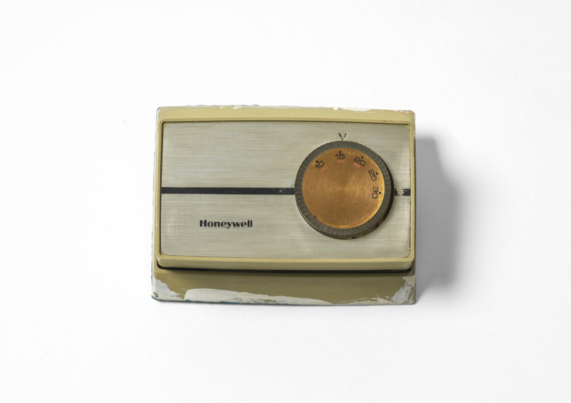 Honeywell thermostat with cream-colored plastic housing and round copper-toned temperature dial.