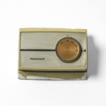 Honeywell thermostat with cream-colored plastic housing and round copper-toned temperature dial.