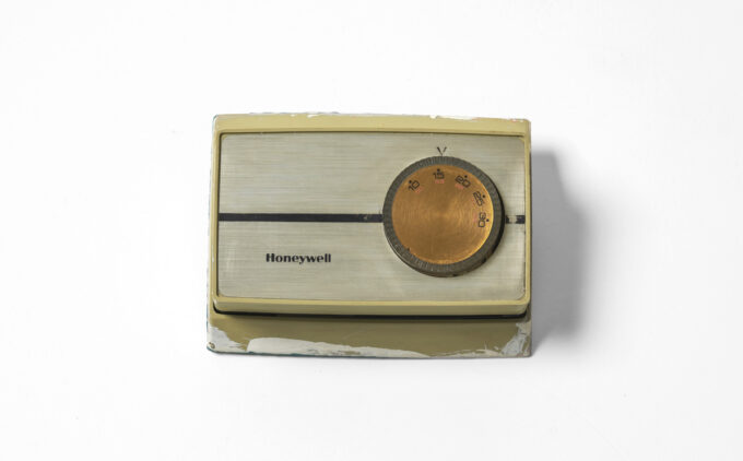 Honeywell thermostat with cream-colored plastic housing and round copper-toned temperature dial.