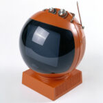 Retro orange spherical television with antenna and control knobs.