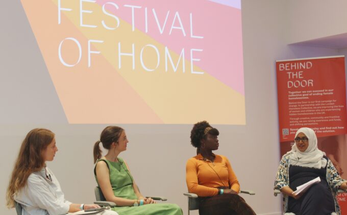 Four women on a panel discussion with colorful backdrop reading 'Festival of Home' and "Behind the Door" campaign banner about female homelessness.