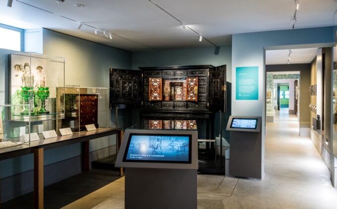 A display featuring cabinets, emerald glassware in display cases, interactive screens and informational plaques