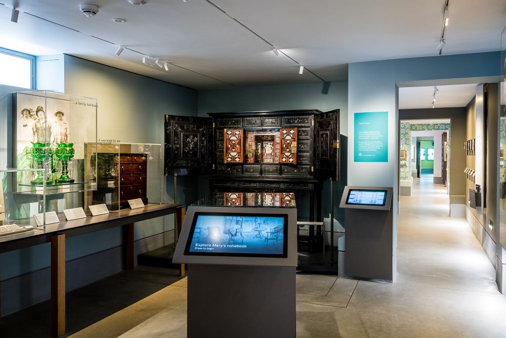 A display featuring cabinets, emerald glassware in display cases, interactive screens and informational plaques