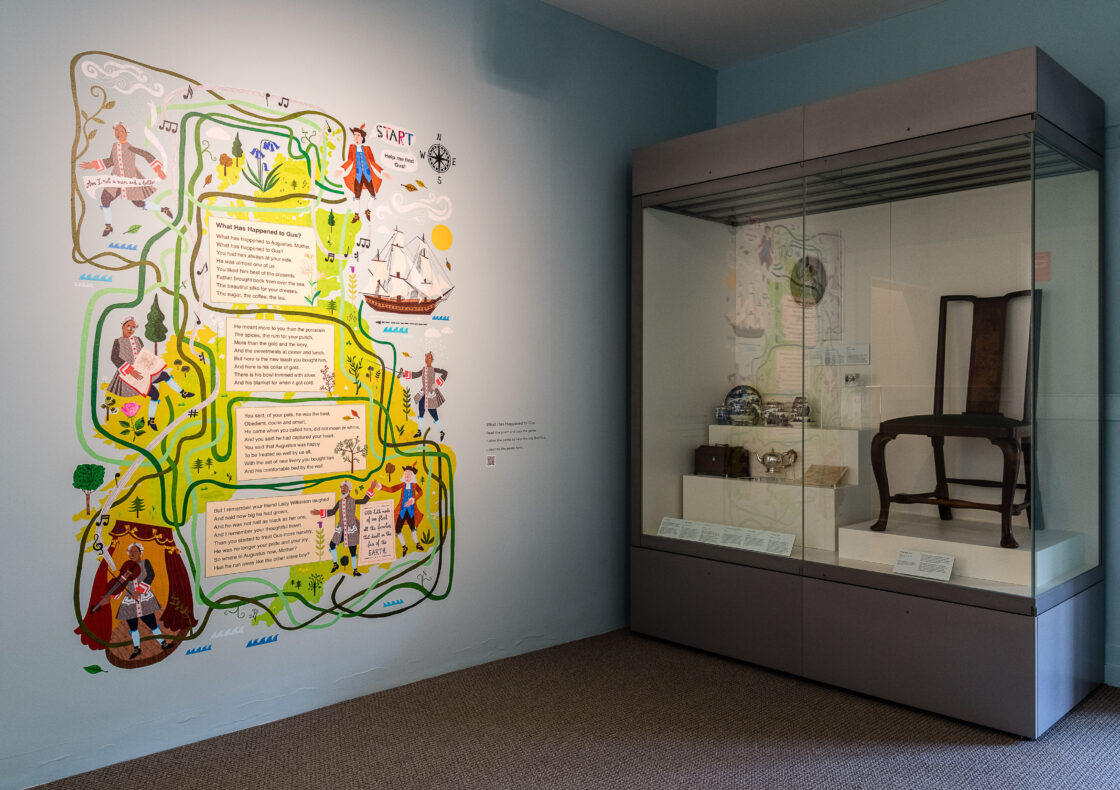 A display featuring a colorful illustrated wall map with characters, ships, and text panels titled "What Has Happened to Gus?" Adjacent is a glass display case containing objetcs.