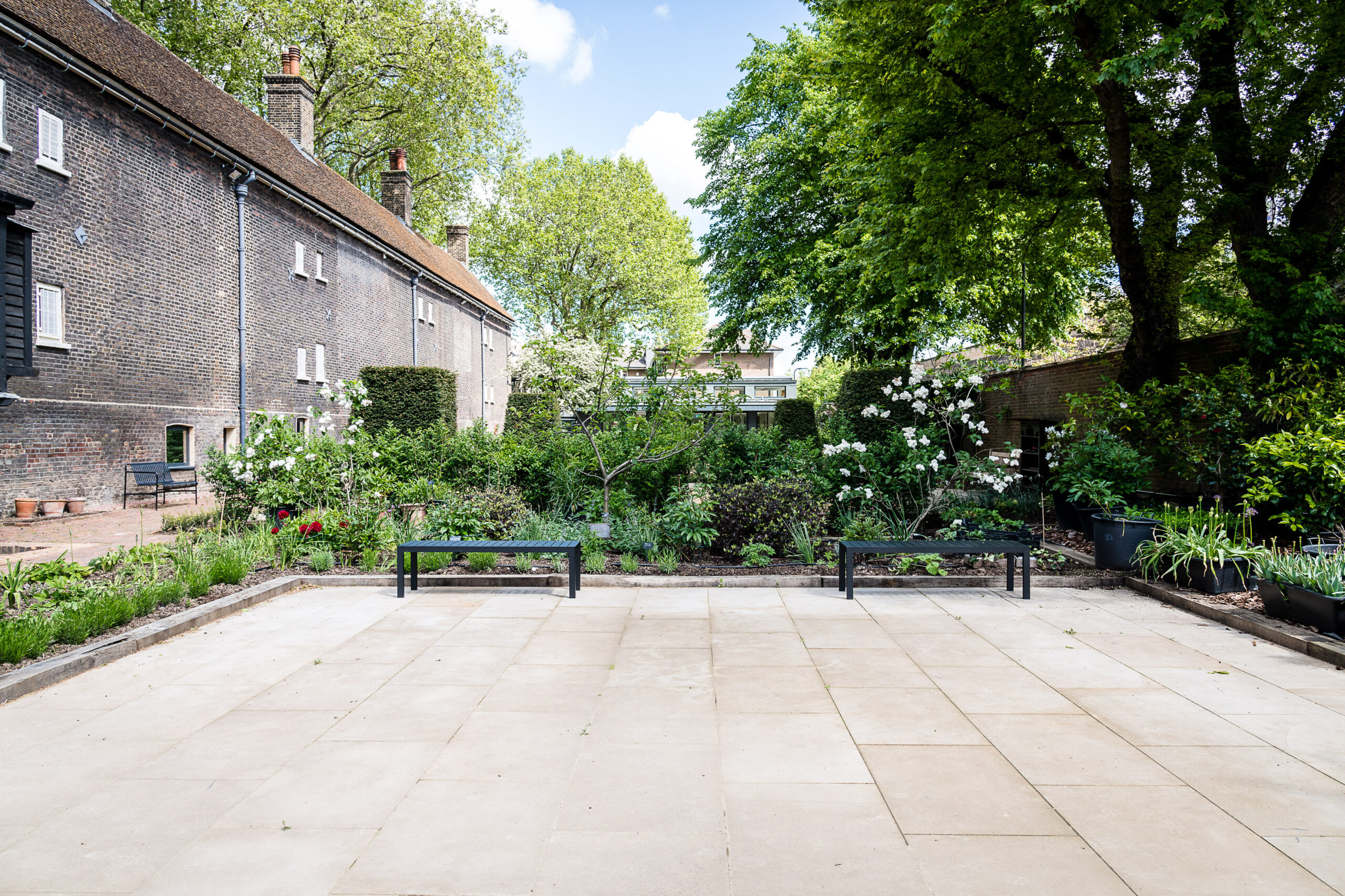 An empty terraced garden with two benches surrounded by trees