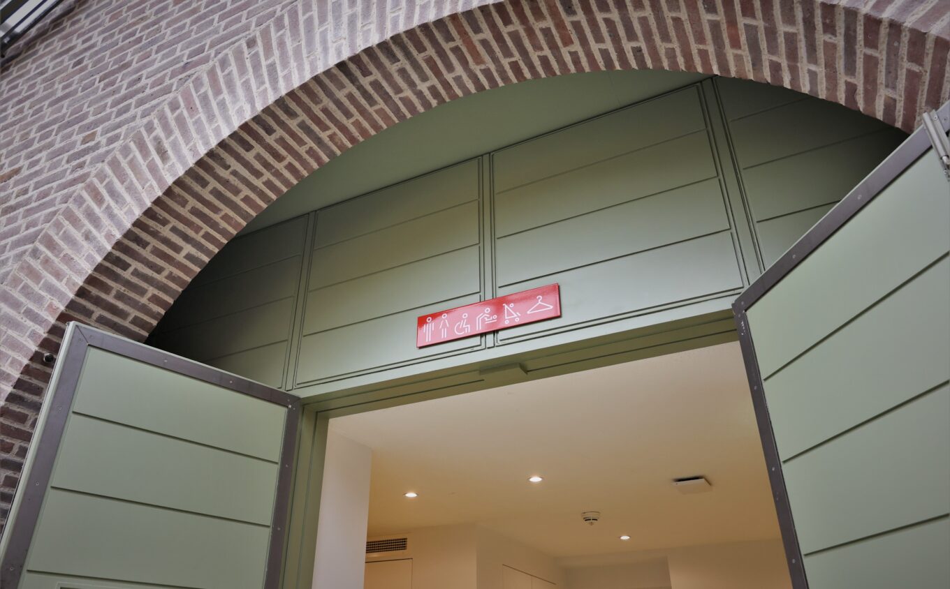 A brick arch with green double doors below and red signage indicating accessible toilets