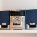 Two blue and grey speakers flank a grey CD player, which features various buttons and knobs.