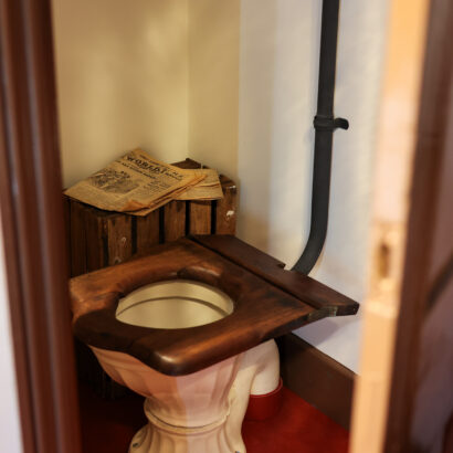 Wooden toilet seat with ceramic basin with a newspaper resting next to it.