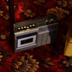 A cassette player and radio with silver and black design sitting on a decorative floral carpet