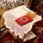 A letter and red item sit on a white lace doily, on a brass table, on a red, floral carpet.